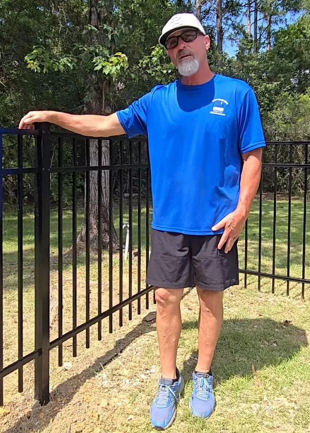 JB, founder of GCG Coastal Fencing, standing next to a black aluminum fence